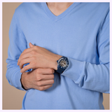 A person in a light blue V-neck sweater wears a Rado Watches Captain Cook High-Tech Ceramic Skeleton R32153209 on their left wrist, its mechanical movement visible, while they gently touch the watch with their right hand.