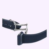 A close-up of a blue textured strap with a stainless steel deployment clasp, designed for the Rado Watches Captain Cook High-Tech Ceramic Skeleton R32153209, shown against a light purple background.