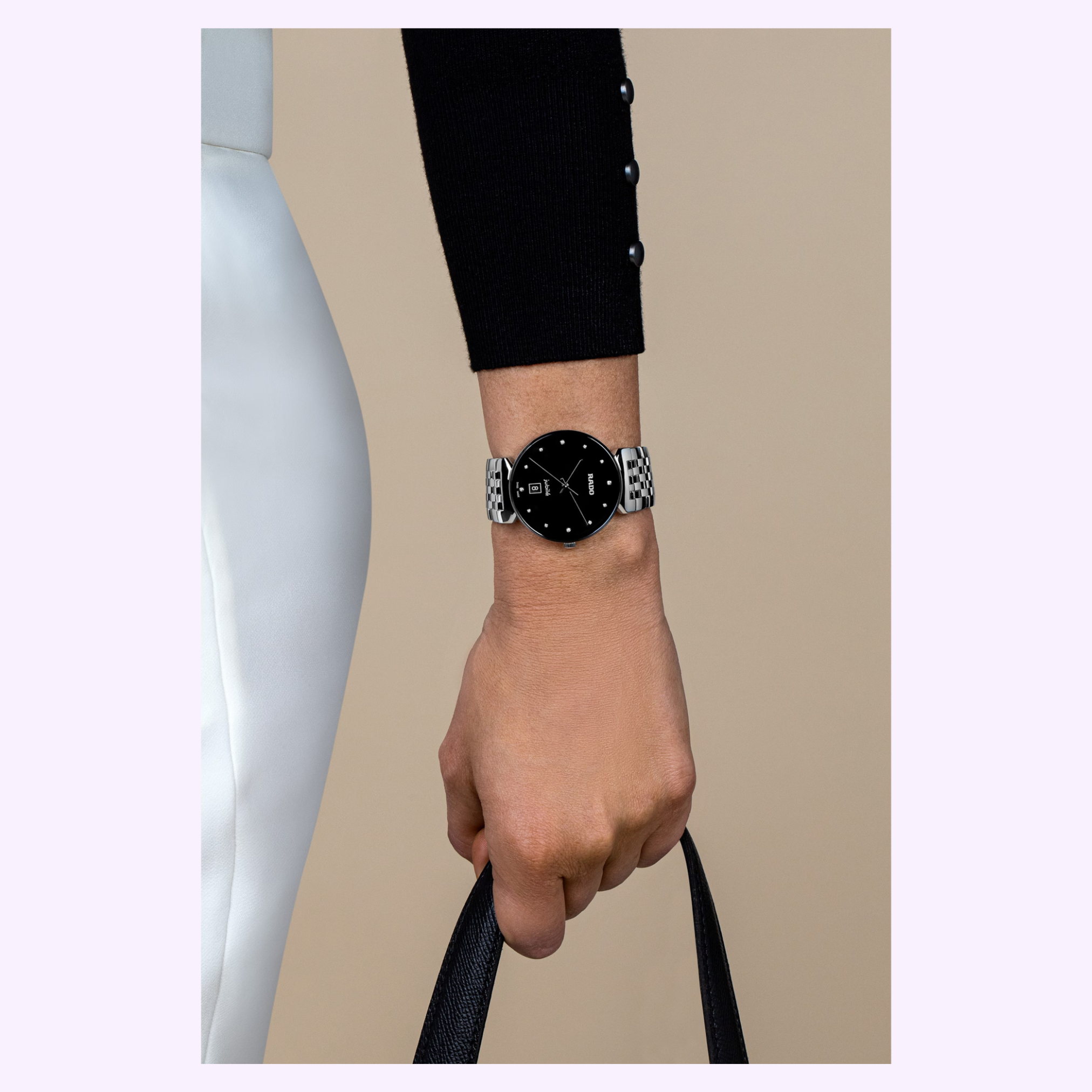 A person in white pants and a black pearl-button top holds a black handbag, wearing a Rado Watches Florence Diamonds R48912733 with a silver and black round face.