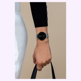 A person in white pants and a black pearl-button top holds a black handbag, wearing a Rado Watches Florence Diamonds R48912733 with a silver and black round face.