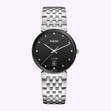 The Rado Watches Florence Diamonds R48912733 features a black dial, silver hour markers, date at 6 o’clock, and a linked stainless steel band, shown against a light purple background.