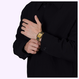 A person wearing a black jacket and a rectangular gold and black Rado Watches Integral Limited Edition R20254702 wristwatch.