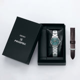A Seiko Luxe Watches PROSPEX ALPINIST SPECIAL EDITION SPB289 with a green dial and silver band is shown in an open black box, highlighting Japanese mechanical craftsmanship. An extra brown leather strap sits beside the box.