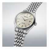 The Seiko Luxe Watches Presage Classic Series SPB463 features a silver case, textured beige dial, date at 3 o’clock, stainless steel bracelet, and highlights Japanese mechanical craftsmanship against a light gradient backdrop.