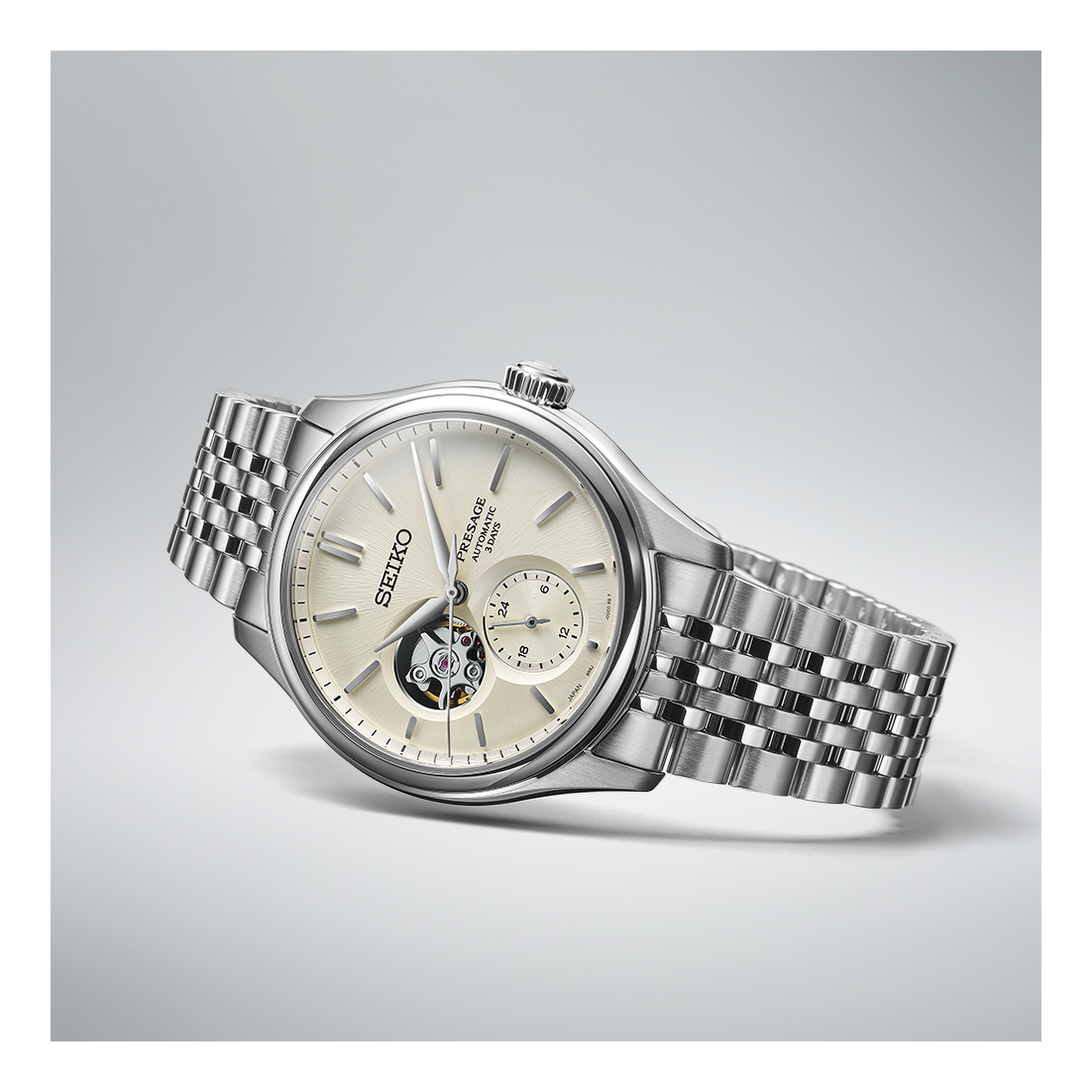 The Seiko Luxe Watches Presage Classic Series SPB469 features a silver stainless steel bracelet, cream dial with open-heart feature, and subdial, elegantly displayed at an angle on a light gray background.