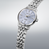 The Seiko Luxe Watches Presage Cocktail Time SRPL61 features a textured light blue dial, silver hands and markers, date window at 3 o’clock, and a stainless steel bracelet—presented on a soft gradient background.