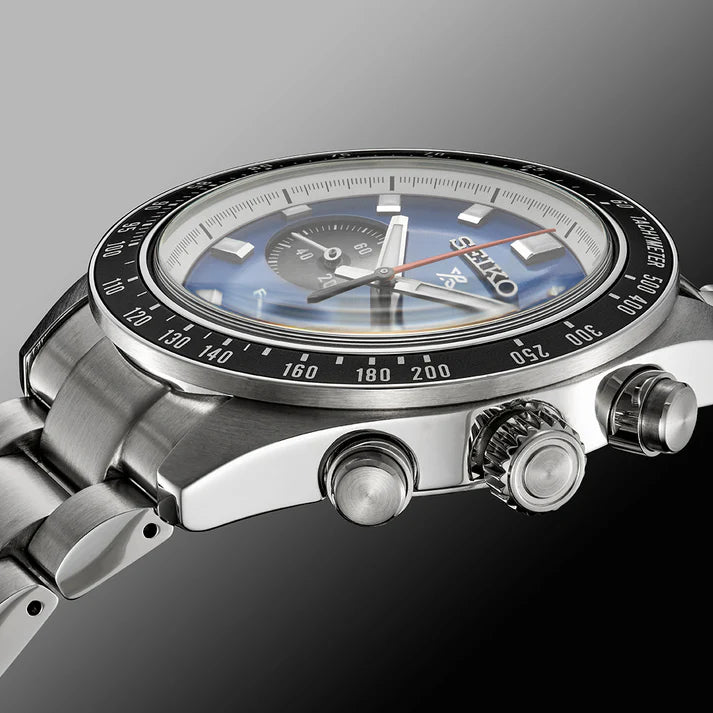 A close-up side view of the Seiko Watches Speedtimer Solar Chronograph SSC931 with a stainless steel band, blue dial, and tachymeter bezel, set against a gradient gray background.