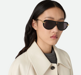 A woman with long dark hair wears Bottega Veneta Sunglasses BV1418S-005 58, a light beige coat, and a gray top, looking confidently at the camera against a plain background.