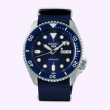 The Seiko Watches SRPD51 Automatic 5 Sports features a deep blue dial with bold white markers and a stainless steel bracelet. The day and date window displays MON 6, while the silver and blue bezel with precise minute markings accentuates the classic design of this 42.5mm timepiece from Seiko Watches.