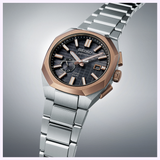 The Seiko King Watches Astron GPS SOLAR SSJ014 by Seiko Luxe Watches features a silver metal band, two-tone rose gold and silver bezel, black textured dial, date display, and rose gold markers and hands.