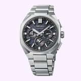 The Seiko Luxe Watches King Astron HAB002 features a stainless steel band, multiple subdials, and a textured blue face, shown against a light purple background.