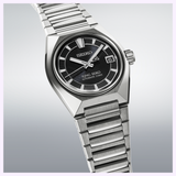 The Seiko Luxe Watches’ King Watches VANAC HKF003 features a stainless steel case, black dial with silver hour markers, and a date window at 3 o’clock; its “King Seiko Automatic 3 Days” inscription highlights sophisticated Japanese watchmaking and the precision of its automatic movement. Shown on a metallic bracelet and photographed at an angle, this model exemplifies the elegance of Seiko’s craftsmanship.