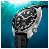 A Seiko Luxe Watches PROSPEX AUTOMATIC DIVER'S WATCH SPB317, featuring a black bezel and strap, is depicted underwater with sunlight streaming down and sharks swimming in the background—a striking tribute to the adventurous spirit of Seiko Luxe Watches.