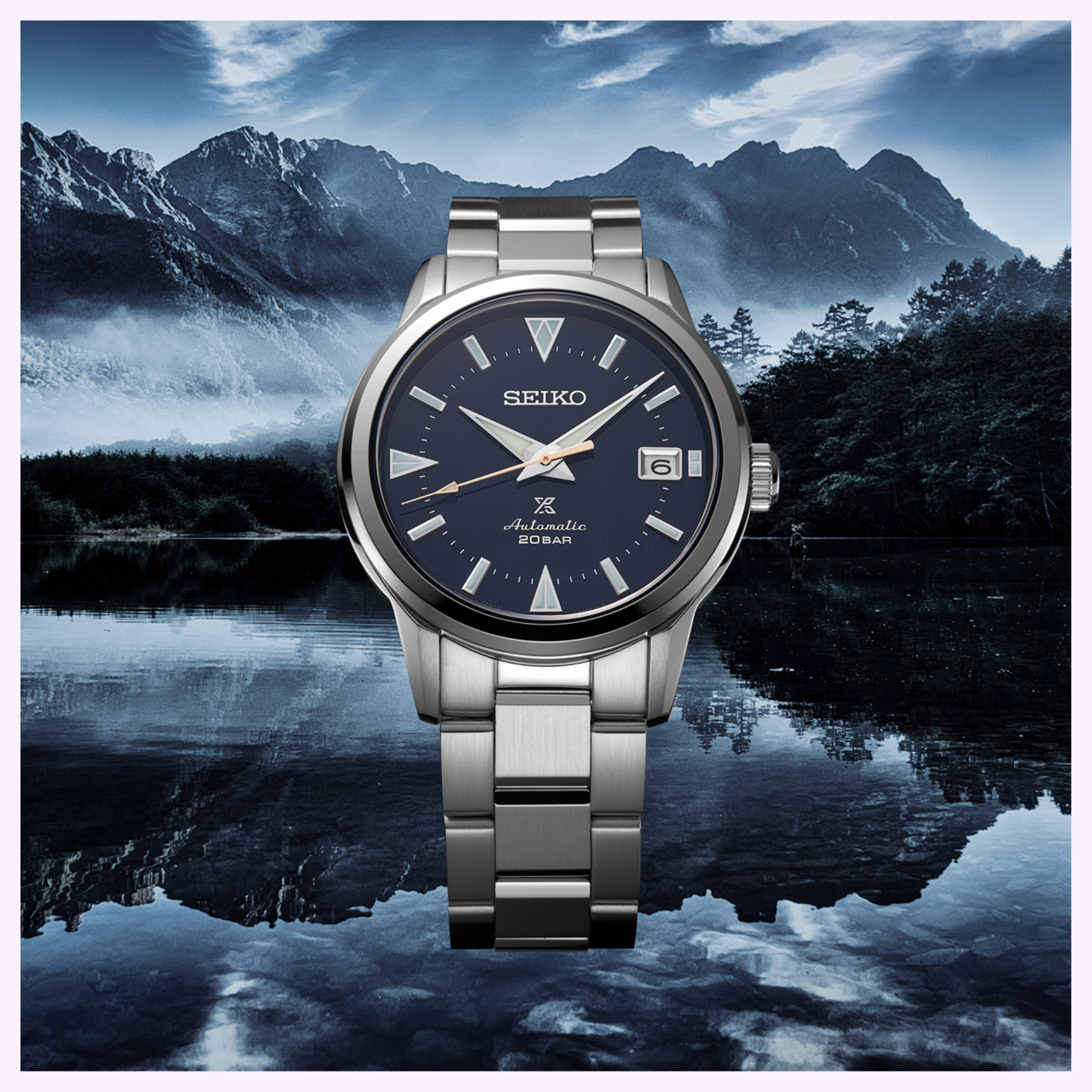 The Seiko Luxe Watches PROSPEX SPB249 automatic watch features a blue dial, silver metal band, date display, and 200m water resistance, shown against a mountain landscape with a reflective lake.