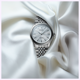 A Seiko Luxe Watches Presage Classic Series HCC001 wristwatch with a silver-tone metal band rests on white, silky fabric, showcasing its elegant, minimalist design and refined dial—a timeless testament to Japanese craftsmanship by Seiko Luxe Watches.