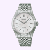 The Seiko Luxe Watches Presage Classic Series HCC001, by Seiko Luxe Watches, showcases exceptional Japanese craftsmanship with its automatic movement, metal link bracelet, silver dial, and minimalist hour markers, beautifully presented against a light purple background.