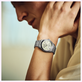 A person wearing a Seiko Luxe Watches Presage Classic Series HCC002 in silver rests their chin on their hand, the green dial from Seiko Luxe Watches’ Classic Series clearly visible. The softly blurred background highlights the watch and hand.