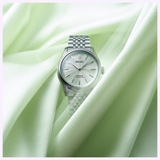 A Seiko Luxe Watches Presage Classic Series HCC002 wristwatch with a silver band and white dial rests on pale green satin fabric, reflecting soft light.