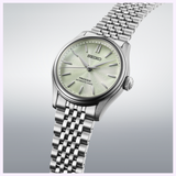 The Seiko Luxe Watches Presage Classic Series HCC002 features a light green textured dial with silver hour markers and a stainless steel bracelet, showcased against a softly gradient backdrop.