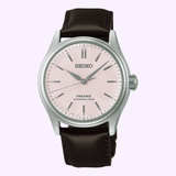 The Seiko Luxe Watches Presage Classic Series HCC003, featuring a Sakura-iro light pink dial with silver hands and markers, a black leather strap, and a sleek silver case, is beautifully presented against a plain light background—a stunning example of Japanese mechanical watch craftsmanship from Seiko Luxe Watches.