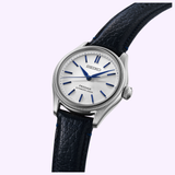 The Seiko Luxe Watches Presage Classic Series HCC004 Limited Edition, a silver automatic with white dial, blue hour markers and hands, and a black textured leather strap, is displayed on a light purple background.