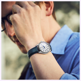 A person in glasses and a blue shirt adjusts their hair, showcasing the Seiko Luxe Watches Presage Classic Series HCC004 Limited Edition on their left wrist. The watch stands out against the softly blurred background.