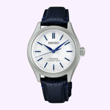 The Seiko Luxe Watches Presage Classic Series HCC004 Limited Edition features a silver dial with blue hour markers and hands, a blue leather strap, and "Presage Automatic 3 Days" on the dial. Set against a light pastel background.