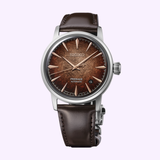 The Seiko Luxe Watches Presage Cocktail Time HCB003 by Seiko Luxe Watches showcases a brown textured dial with rose gold markers, set in a silver case and paired with a brown leather strap, all elegantly displayed on a light background.