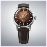 The Seiko Luxe Watches Presage Cocktail Time HCB003 showcases a textured brown dial, silver hands and markers, a date window at 3 o’clock, and a brown leather strap. Elegantly presented against a light gray gradient background, this automatic timepiece embodies the sophistication of Seiko Luxe Watches.