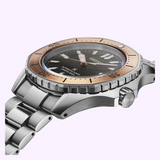 Close-up of the Seiko Luxe Watches Prospex Sea SPB485 diver watch by Seiko Luxe Watches, featuring a metallic band, black dial, large luminous markers, and rose gold bezel against a light purple background.