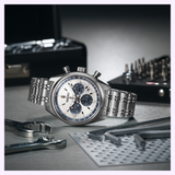 A Seiko Luxe Watches Prospex Speedtimer Mechanical Chronograph SRQ047 with a silver and blue dial rests on a metal surface, surrounded by wrenches, hex keys, and a toolkit in the background.