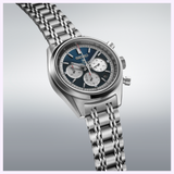 The Seiko Luxe Watches Speedtimer SRQ051 by Seiko Luxe Watches is a silver chronograph watch featuring a blue and silver dial with three subdials, powered by the precise Caliber 8R48 mechanical chronograph movement, and completed with a metal link bracelet, displayed on a light gradient background.