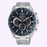A Seiko Watches SSB345 Chronograph men’s watch by Seiko Watches, showcasing a silver stainless steel link band, a blue tachymeter bezel, and three subdials, displayed against a light purple background.