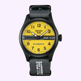 Seiko Watches 5 Sports Field series HDB010 Honda MOTOCOMPO Limited Edition analog wristwatch with a bright yellow face, black numerals, a gray center stripe, a day-date window, and a gray nylon strap with white lettering.