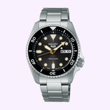 The Seiko Watches 5 Sports SKX series SRPL79 features a black dial with gold accents, silver hour markers, day-date display set to Monday the 6th, a rotating bezel, and a gold stainless steel bracelet.