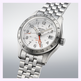 The Seiko Watches 5 Sports SSK059, featuring a silver dial, silver metal band, date display at 3 o’clock, and a striking orange GMT hand, is photographed against a light gradient background—making it an outstanding addition to the Field Series of GMT watches from Seiko Watches.
