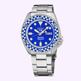 The Seiko Watches 5 Sports X Rowing Blazers SRPM19 Limited Edition features a silver band, a blue and white checkered bezel, a blue dial with yellow markers and hands, “Rowing Blazers” written above the 6 o’clock position, and displays the day and date at 3 o’clock. This exclusive timepiece is part of the Rowing Blazers Limited Edition collection by Seiko Watches.