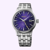 Introducing the Seiko Watches Presage Cocktail Time HCB006 145th Anniversary Limited Edition—a striking silver wristwatch by Seiko Watches, featuring a deep Edo Purple sunburst dial, silver hour markers, a date window at 3 o’clock, and a sophisticated metal bracelet. Presented against a light lavender background, this captivating limited edition timepiece is sure to appeal to any watch enthusiast.