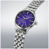 The Seiko Watches Presage Cocktail Time HCB006 145th Anniversary Limited Edition features a striking Edo Purple dial, silver hour markers, a date window at 3 o’clock, and a stainless steel bracelet, showcased against a light gray background.