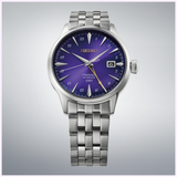 A Seiko Watches Presage Cocktail Time HCB006 145th Anniversary Limited Edition watch featuring a silver metal band, an eye-catching Edo Purple textured dial, gold GMT hand, and a date window at 3 o’clock, showcased against a light gray gradient background.
