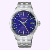 The Seiko Watches Presage Cocktail Time HCB006 145th Anniversary Limited Edition boasts a striking blue face with gold accents, a date window at 3 o’clock, silver hour markers, and a stainless steel bracelet, elegantly showcased against a light background.