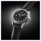 The Seiko Luxe Watches Prospex Alpinist GMT SPB379 features a black dial, silver case, black leather strap, and dual crowns. Its face showcases Arabic numerals, a red-tipped second hand, and prominent GMT markings—all signature elements of an elegant GMT timepiece—set against a sophisticated dark gradient background.