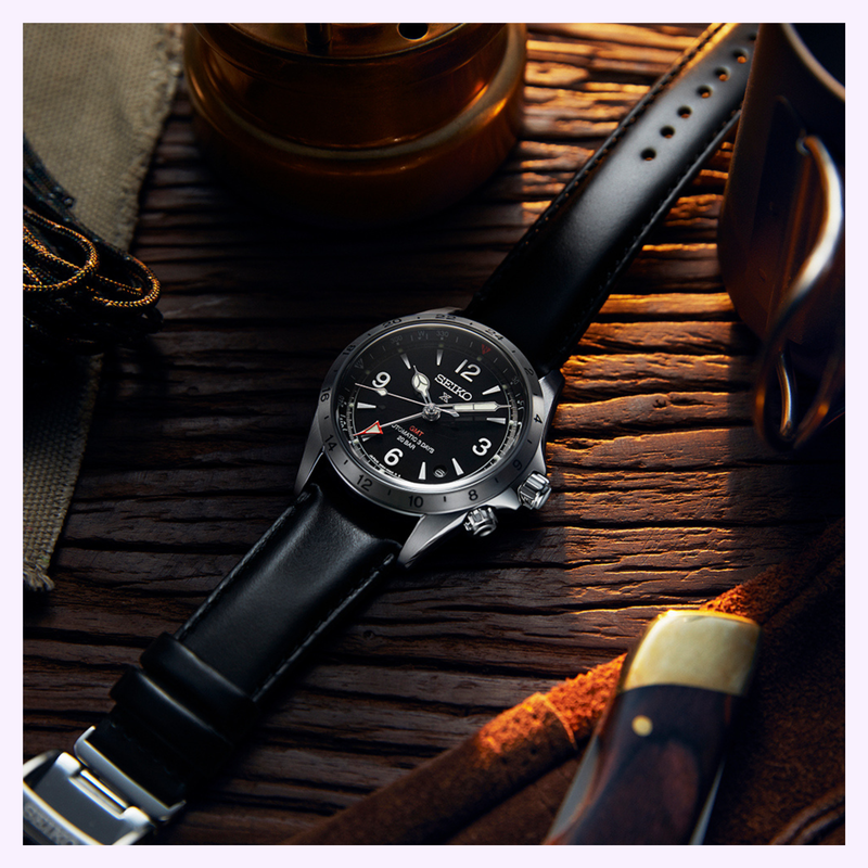 Seiko Prospex Alpinist GMT SPB379 watch with black leather strap resting on a rustic wooden table beside outdoor gear