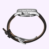 A side view of a Seiko Watches Prospex Alpinist HBC007 by Seiko Luxe Watches, featuring a round silver case, two pushers, a black dial leather strap, and quartz movement, set against a light purple background.