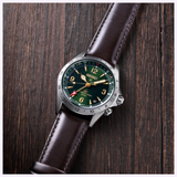 A Seiko Luxe Watches Prospex Alpinist HBC007 wristwatch with a green dial, gold accents, and brown leather strap rests on a wooden surface. Featuring precise Seiko quartz movement, the watch displays the time and date, and has a red arrow on the bezel.