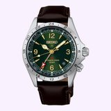 The Seiko Watches Prospex Alpinist HBC007 by Seiko Luxe Watches features a dark green dial, silver bezel, gold accents, and a brown leather strap. This reliable quartz watch displays the time, date, and GMT function with a red-tipped hand.