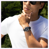 A person wearing sunglasses and a white t-shirt, with their hand to their chin, showcasing a Seiko Watches Prospex Speedtimer Mechanical HBC004 chronograph wristwatch with a black face and leather strap.