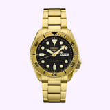 The Seiko Watches SRPK18 Seiko 5 Sports SGP features a gold case and bracelet, black dial with gold hands, round and rectangular markers, day-date display at 3 o’clock, shown against a light purple background.
