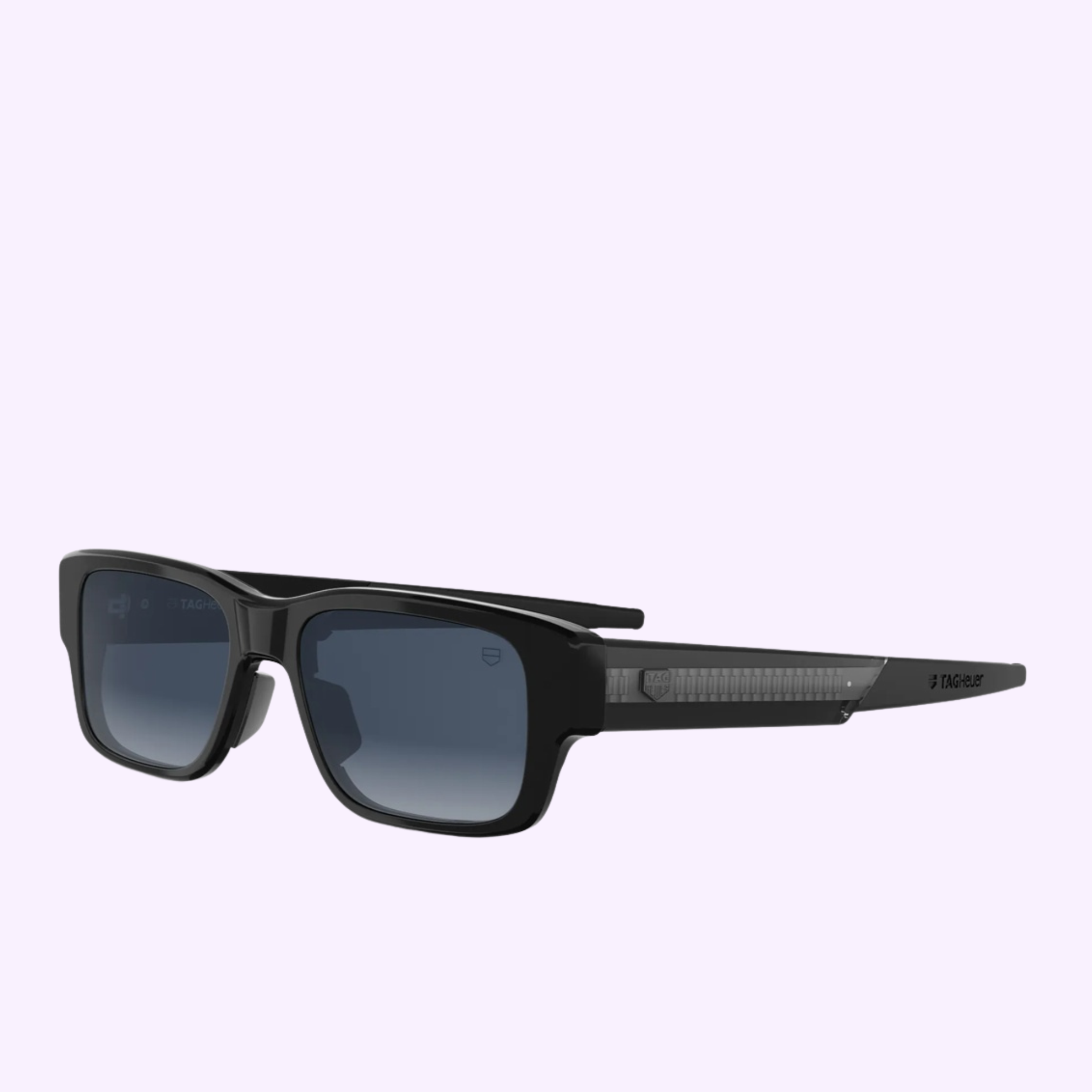 The Tag Heuer Optical Sunglasses TH40061I 5401W are displayed in a bold black rectangular design with dark lenses and chunky frames, set against a light purple backdrop. The arms feature textured detailing and discreet branding near the hinge, adding a contemporary flair ideal for Miami’s energetic atmosphere.