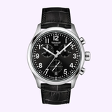 The Tissot Watches Chrono L 42mm T1164171605200 features a black leather strap, a black dial with silver hands, three subdials, a date window at 4 o’clock, and a stainless steel case showcased on a light purple background. This elegant 42mm timepiece by Tissot Watches is powered by Swiss Quartz movement for reliable precision.